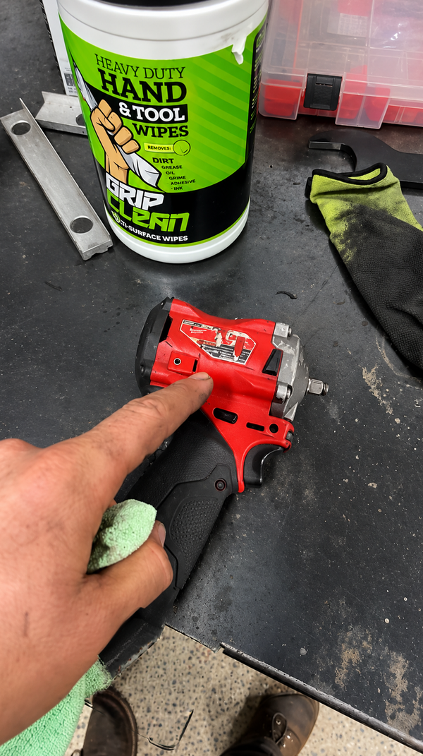 Mechanic cleaning a greasy cordless impact wrench with a Grip Clean heavy duty hand and tool wipe, canister on the workbench
