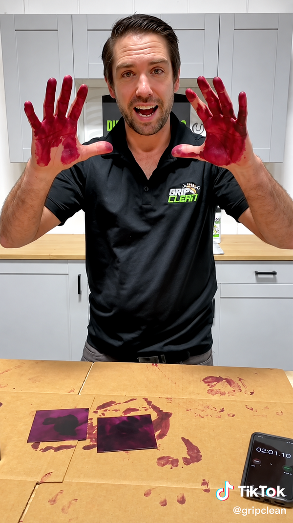 Man holding up both hands stained deep red with leather dye before testing Grip Clean, with a timer and dyed leather samples on the table